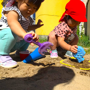 砂場で遊ぶ2人の幼児。一人はシャベルを、もう一人は魚の形をした砂型を持っている