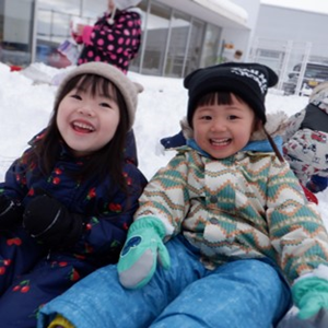 雪の中で遊ぶ2人の子供たち。2人とも冬の服装をしており、笑顔でカメラを見つめている