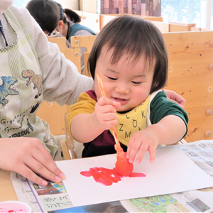 筆を使って紙に絵の具を塗っている幼い子ども