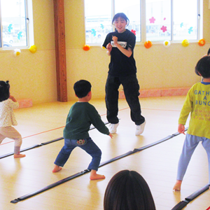 広々とした室内で、保育士と思われる女性が数人の子どもたちと遊んでいる様子