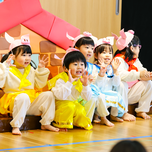舞台の上で子豚の耳をつけて衣装をまとい、大きな口を開けて元気に劇の練習やお遊戯をする子どもたち。
