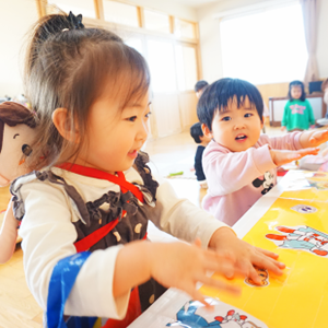 明るい室内で、テーブルに並んだカードやおもちゃを前にして、目を輝かせて遊んでいる子どもたちの表情。