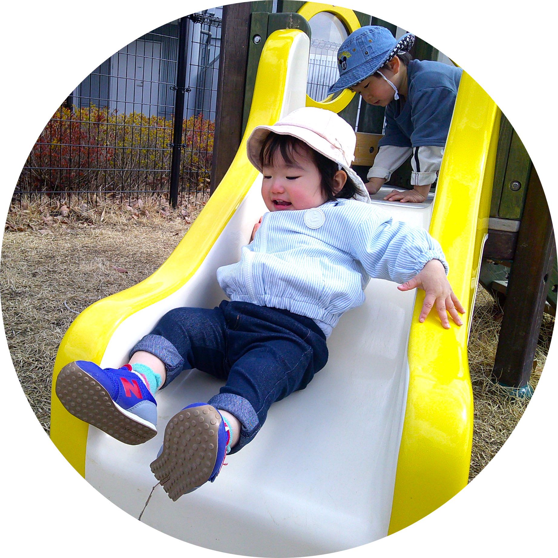 黄色い滑り台を滑り降りる女の子と、後ろで見守る男の子。