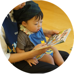 保育士の膝の上で、一緒に絵本を読んでいる男の子の様子。