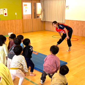 広い多目的室で、指導員の先生の動きを真似しながら、マットやフープを使って一生懸命に準備体操や運動に取り組む子どもたち。
