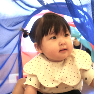 透き通った青い布のトンネルをくぐり抜け、不思議そうな表情で周りを見渡している可愛らしい女の子。